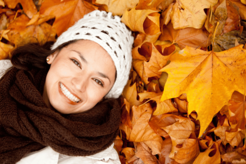 Woman with youthful, bright skin enjoying the fall weather in a pile of autumn leaves